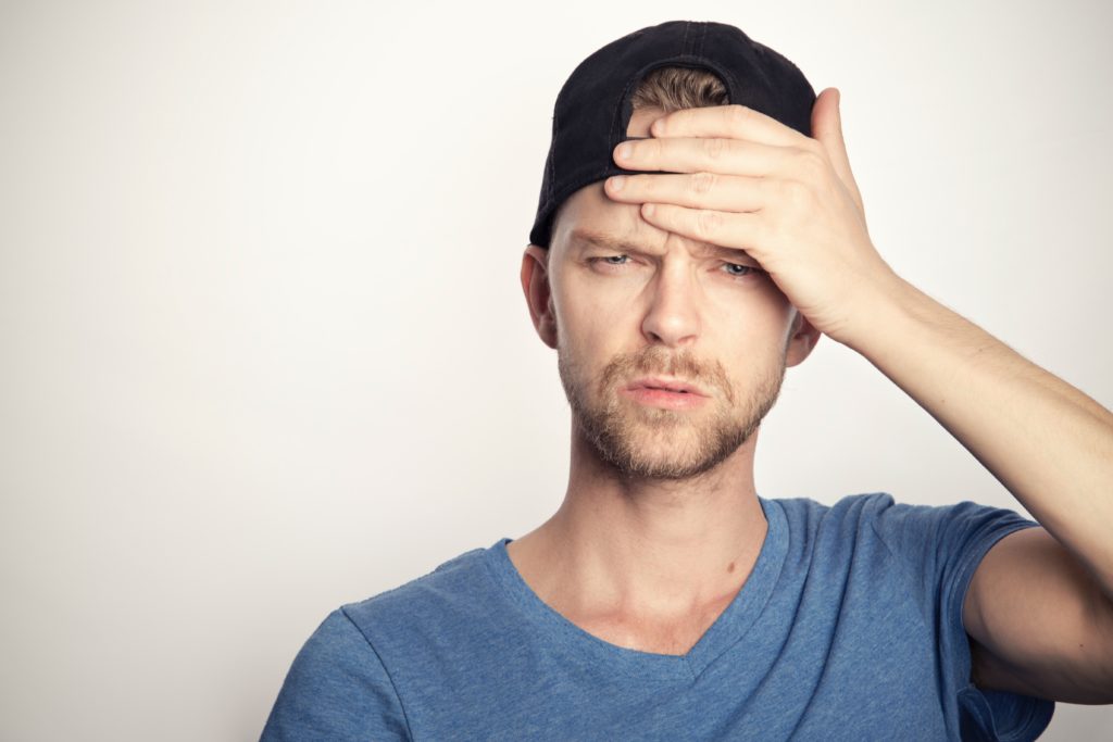 man in blue crew neck shirt covering forehead with hand looking confused
