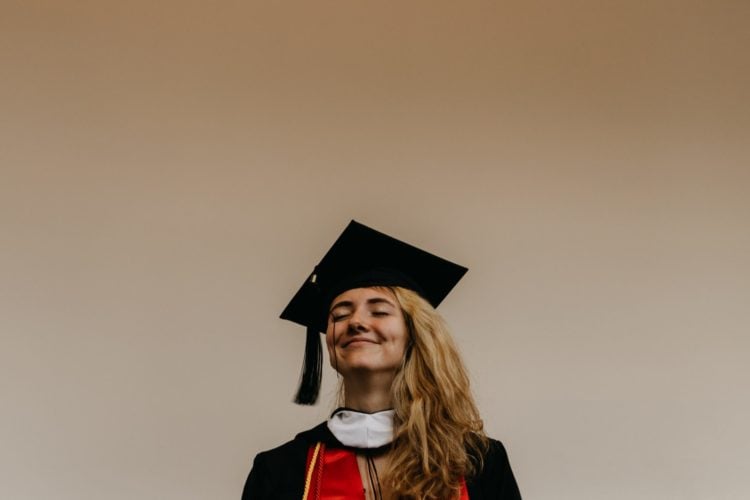 young woman in black and red graduate dress stood against white wall